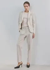 Blazer sastre entallado color beige, con cuello en pico, solapas de muesca, manga larga y bolsillos con solapa en la parte delantera.