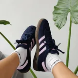 Championes Adidas Handball Spezial de corte bajo, confeccionados en gamuza negra con detalles en rosado en las icónicas tres tiras, cordones y talón. Presenta una suela de caucho color caramelo y el logo de la marca en dorado en el lateral.