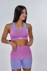 Conjunto deportivo compuesto por un top y un short de ciclismo, ambos con diseño degradado que transiciona de fucsia a lila. El top presenta cuello redondo y logo 'bk.' estampado en el frente, mientras que el short es de tiro alto y ajuste ceñido.