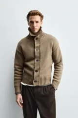 Chaqueta de punto de corte relajado, color marrón, con cuello subido, manga larga y cierre frontal de botones. Presenta acabados en rib en puños y ruedo.
