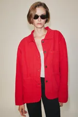 Chaqueta oversize de corte recto en color rojo, con cuello solapa, manga larga y bolsillos de parche delanteros. Cuenta con cierre frontal de botones metálicos y pespuntes a contraste.