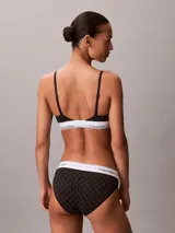 Bralette Calvin Klein de corte triangular, color negro con estampado geométrico de monogramas y banda elástica inferior blanca con el logotipo de la marca. Cuenta con tirantes finos ajustables.