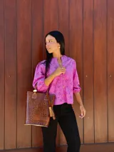 Matera de cuero con textura de cocodrilo en color tostado, con asas cortas y detalle de borla decorativa lateral.