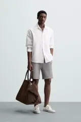 Bermuda negra de corte recto, con cintura elástica ajustable mediante cordón, pliegues frontales y bolsillos de vivo en la espalda. El bajo tiene un dobladillo vuelto.