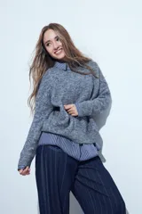 Sweater de tejido de punto gris con textura, de calce relajado y manga larga. Presenta un diseño sutil de líneas bordadas en color azul que recorren la prenda.