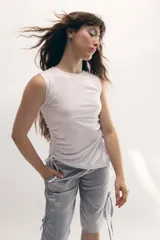 Musculosa blanca elastizada asimétrica y sin mangas, con jaretas laterales regulables que permiten ajustar el largo y el volumen.
