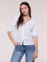 Blusa blanca de calce holgado, con bordado en relieve tipo broderie de motivos florales en toda la prenda. Presenta escote en V con fruncido en los hombros, cierre frontal con botonadura y mangas tres cuartos abullonadas con puños elastizados.