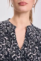 Vestido corto de manga corta y cuello mao con abertura en V, de corte suelto y estampado floral o abstracto en tonos beige sobre fondo negro.