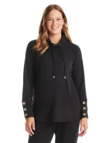 Buzo de tejido suave con cuello volcado ajustable mediante cordones con punteras metálicas doradas. Presenta mangas largas con puños anchos decorados con botones metálicos, hombros caídos y ruedo redondeado con aberturas laterales.