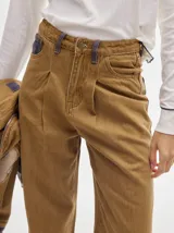 Pantalón jean de tiro alto y corte pinzado, con perneras de caída suelta y levemente anchas en el bajo. Posee pasador con hebilla en la parte trasera.