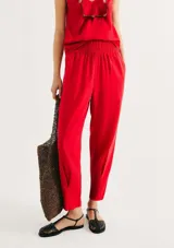 Pantalón de lino color rojo, de corte holgado y talle alto con cintura elástica fruncida. Presenta diseño recto que se estrecha ligeramente hacia los tobillos.