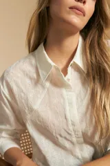 Camisa blanca de manga larga con textura calada o bordada, cuello camisero y corte holgado.