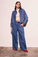 Camisa de jean azul de corte recto, con cuello clásico, cierre frontal con botones marrones, bolsillo de parche en el pecho y mangas largas con puños abotonados.