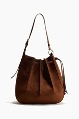 Cartera bandolera de gamuza color marrón, con diseño de pliegues cosidos y cordón ajustable en la parte superior. Cuenta con correa de hombro ajustable y herrajes metálicos.