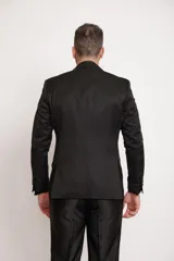 Ambo de corte slim fit compuesto por saco y pantalón. El saco presenta un tejido con sutiles patrones brillantes, solapas satinadas y bolsillos con ribete satinado. Se complementa con una camisa negra, moño blanco y pañuelo de bolsillo blanco.