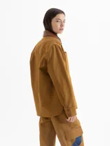 Chaqueta color marrón confeccionada en gabardina, con cuello y cartera de cuero marrón. Presenta broches a tono de cuero en la cartera y puños, bolsillos plaqué y sastreros en el delantero. Incluye volados de denim azul que aportan un toque original al diseño.