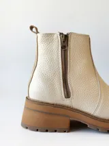 Bota corta de cuero vacuno con textura granulada, color crudo. Presenta cierre lateral metálico, suela track de goma en tono suela y tirador trasero.