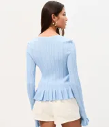 Saco de tricot celeste con textura acanalada vertical, escote en V y cierre frontal con lazos atables. Presenta mangas largas con puños acampanados con volados, al igual que el ruedo.