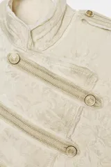 Chaqueta corta de estilo militar con cuello alto y manga larga. Confeccionada en tejido jacquard con diseño floral, presenta botones metálicos en relieve en el cierre frontal, hombros y puños. Incluye trabillas en los hombros, forro interior y acabados desflecados.