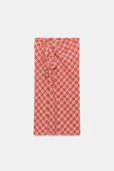 Falda midi de tiro medio ZARA WOMAN COLLECTION confeccionada en hilatura con algodón, con estampado de cuadros en tonos rojos y blancos. Presenta detalle de pliegue con lazadas en el delantero y bajo recto con abertura. Cierre con cremallera oculta en costura.