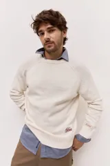 Sweater de punto color off white con cuello redondo, manga larga y detalle de bordado y parche con logo en la manga.