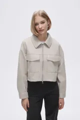 Chaqueta de eco-cuero en color beige, con diseño holgado, cuello tipo camisa y cierre frontal metálico. Presenta dos bolsillos frontales con solapa y mangas largas con puños rectos.