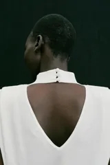 Top de punto blanco sin mangas con cuello subido, hombreras marcadas y espalda descubierta con cierre de botones.
