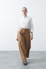 Camisa de color celeste claro con silueta relajada y mangas largas. Presenta un cuello redondo con pequeña abertura frontal y botones, además de un delicado trabajo de tablas en los hombros que aporta textura al diseño.