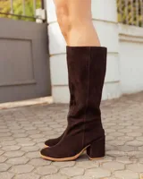 Botas altas de caña recta confeccionadas en cuero con acabado de gamuza, color marrón chocolate, tacón ancho y bloque, y punta redondeada.