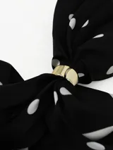 Pañuelo cuadrado de tela ligera color negro con estampado de lunares blancos y borde con franja blanca. Incluye un anillo metálico dorado para sujetar y estilizar el pañuelo.