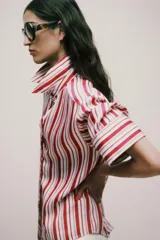 Camisa de cuello solapa con estampado de rayas verticales en tonos rojos, rosas y blancos. Presenta cierre frontal con botones y mangas por debajo del codo con terminación en vuelta.