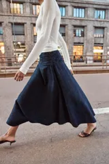 Falda midi de tiro alto con detalle de frunces en la cintura y bajo asimétrico. Presenta cierre lateral con cremallera oculta.