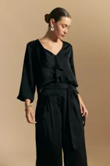 Blusa negra de satén con escote en V y detalle de volados frontales. Presenta mangas largas con puños abotonados y una silueta fluida.