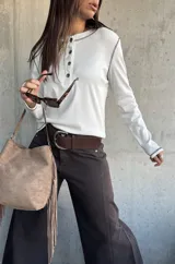 Remera de manga larga en color blanco, confeccionada en tejido acanalado. Presenta un diseño tipo henley con cuello redondo y una pequeña botonadura frontal, destacada por costuras a contratono en color oscuro que recorren los hombros y los puños.