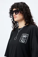 Remera blanca de corte amplio con mangas cortas y estampado de una postal con una palmera y el mar.