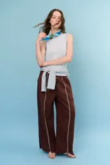 Pantalon de lino color marrón con costuras blancas decorativas a lo largo de las piernas y corte amplio.