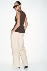 Top de punto acanalado en color beige, sin mangas y con cuello redondo. Presenta un cierre frontal con botones pequeños y un bajo con acabado en peplum que aporta volumen.