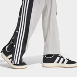 Pantalón deportivo Adidas Adibreak de color gris, con franjas negras laterales y las clásicas tres tiras blancas. Cuenta con botones a presión en los laterales, cintura elástica y diseño holgado.