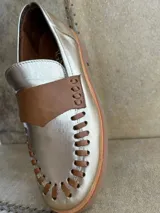 Mocasines de cuero en color dorado con detalles en marrón, con diseño bicolor y costuras artesanales expuestas en el empeine.
