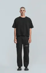 Pantalón cargo negro de corte recto y holgado, con bolsillos grandes con solapa en los laterales de las piernas y un pequeño parche blanco con texto en uno de ellos.
