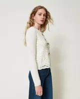 Chaqueta de hilo color crema con cuello redondo, mangas largas y cierre frontal con botones dorados. Diseño calado de crochet en la parte delantera y trasera.