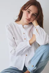 Blusa de lino color blanco, con cuello redondo, manga larga y cierre frontal con botones de madera. Presenta dos bolsillos frontales tipo parche con costuras a la vista.
