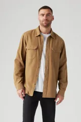 Camisa color marrón claro de corte clásico, con cuello abotonado, cierre frontal con botones, dos bolsillos de parche con botón en el pecho y mangas largas con puños abotonados.