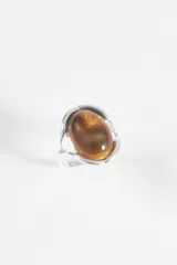 Anillo de metal plateado con diseño envolvente y piedra central ovalada en tono ámbar con destellos dorados.