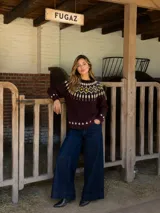Buzo tejido en lana merino con diseño nórdico, de color bordó con guardas decorativas en tonos manteca y mostaza en el cuello y puños. Presenta un corte clásico de cuello redondo y mangas largas.