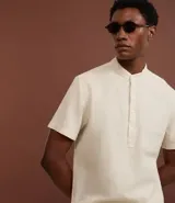 Camisa de manga corta confeccionada en mezcla de lino y algodón, con cuello tipo padre y cierre frontal parcial con botones.