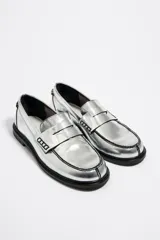 Mocasines plateados de cuero sintético con detalle de antifaz y suela plana negra.