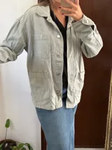 Campera de jean verde claro de corte oversize, con bolsillos frontales con solapa en el pecho y bolsillos aplicados en la parte inferior. Cierre frontal con botones metálicos y cuello camisero.