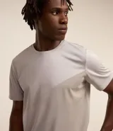 Remera deportiva de hombre, color gris claro, con cuello redondo y manga corta. Presenta un sutil efecto degradado o panel de color más claro en la zona del pecho.