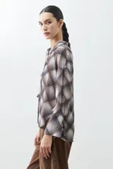 Camisa de manga larga con estampado escocés en tonos chocolate, blanco y gris. Presenta cuello camisero, cierre frontal con lazos y puños con lazos ajustables.
